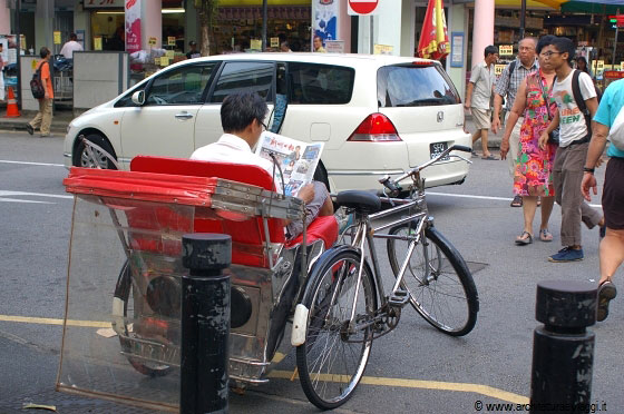 SINGAPORE - Un guidatore di risciò legge tranquillamente il giornale in attesa di clienti di fronte a Bugis Street