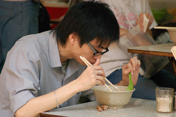 WAN CHAI - Dal nostro tavolino fotografiamo questo cinese mentre pranza all'interno del dai pai dong di fronte a noi, gustando un piatto di tagliolini in brodo con bacchette e cucchiaio