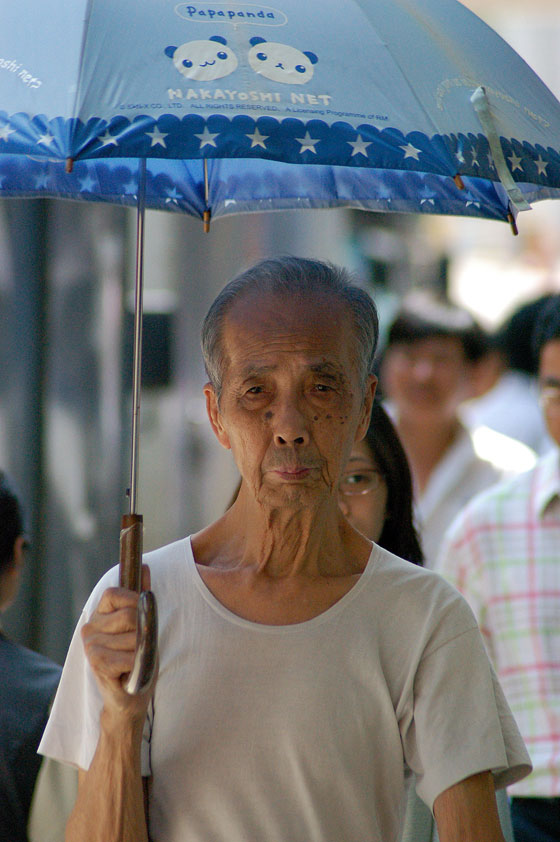 WAN CHAI - Sembra una vera e propria sfilata di personaggi quelli che osserviamo passare: quest'anziano cinese con il suo parasole 