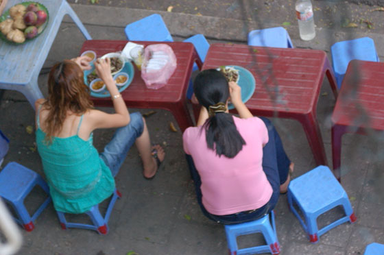 HANOI - Giovani donne mangiano sui marciapiedi sedute su sgabelli