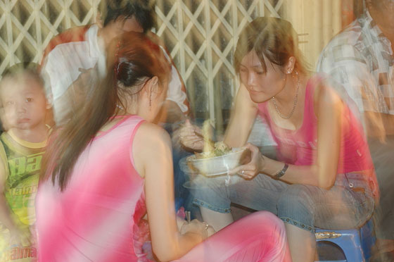 HANOI - Giovani vietnamite mangiano su un marciapiede nei pressi del mercato notturno