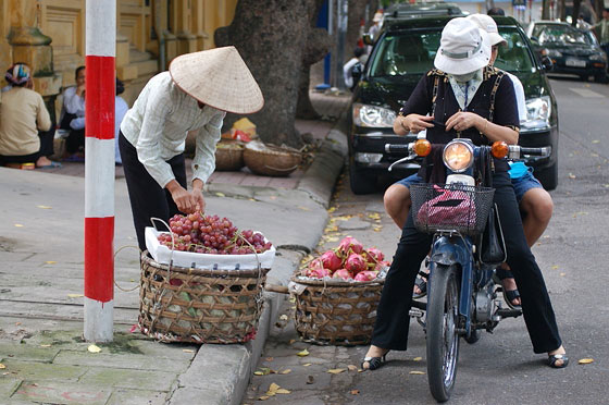 HANOI - Due donne in motorino si fermano a comprare frutta da una venditrice ambulante